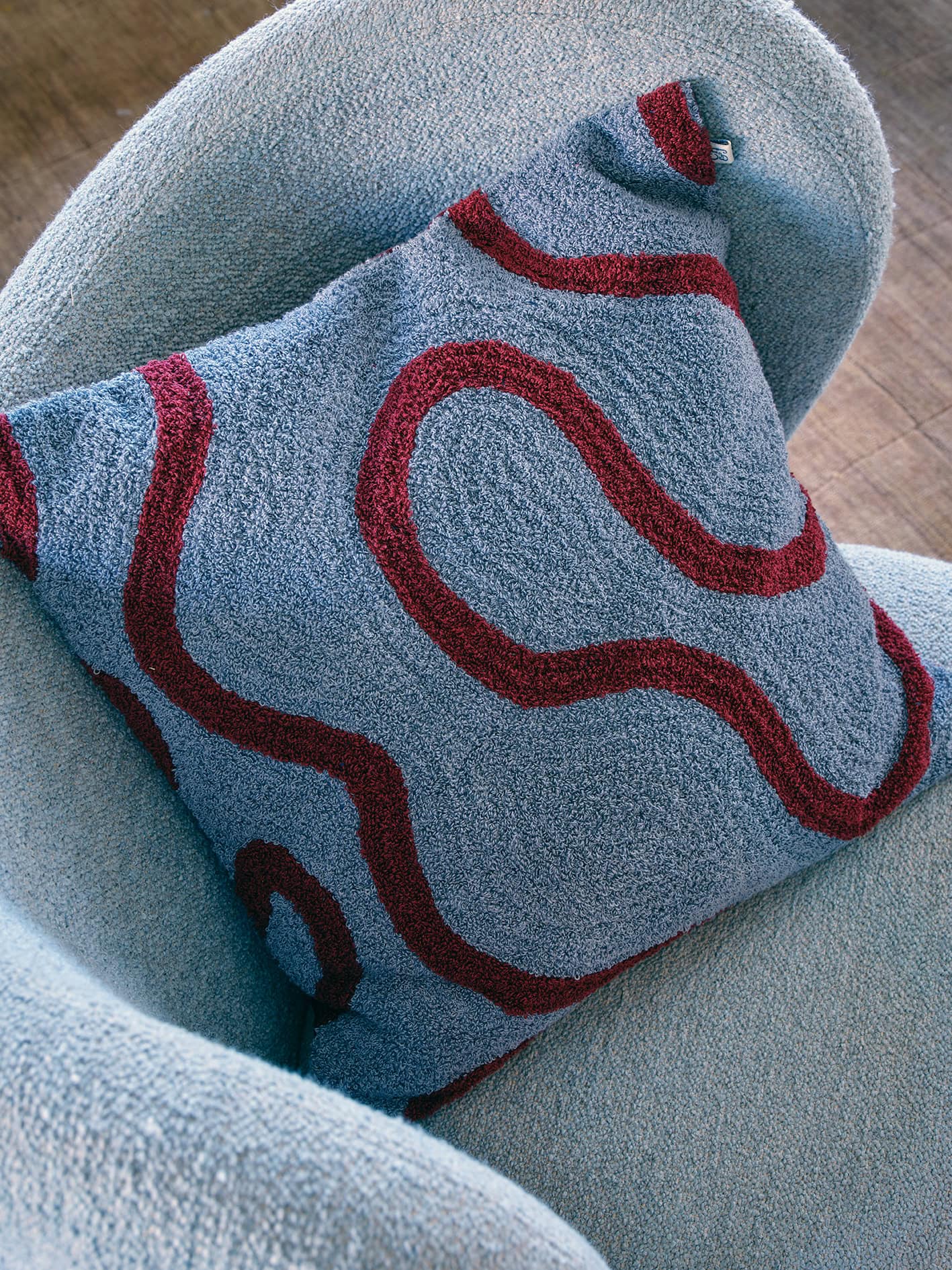 Blue and ruby coloured designer boucle cushion in a blue armchair